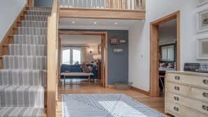 A spacious living area with a wooden staircase, a sofa set, and a dining table. - Highfield - 3 Bedroom Holiday Home - Llanmadoc (Swansea)