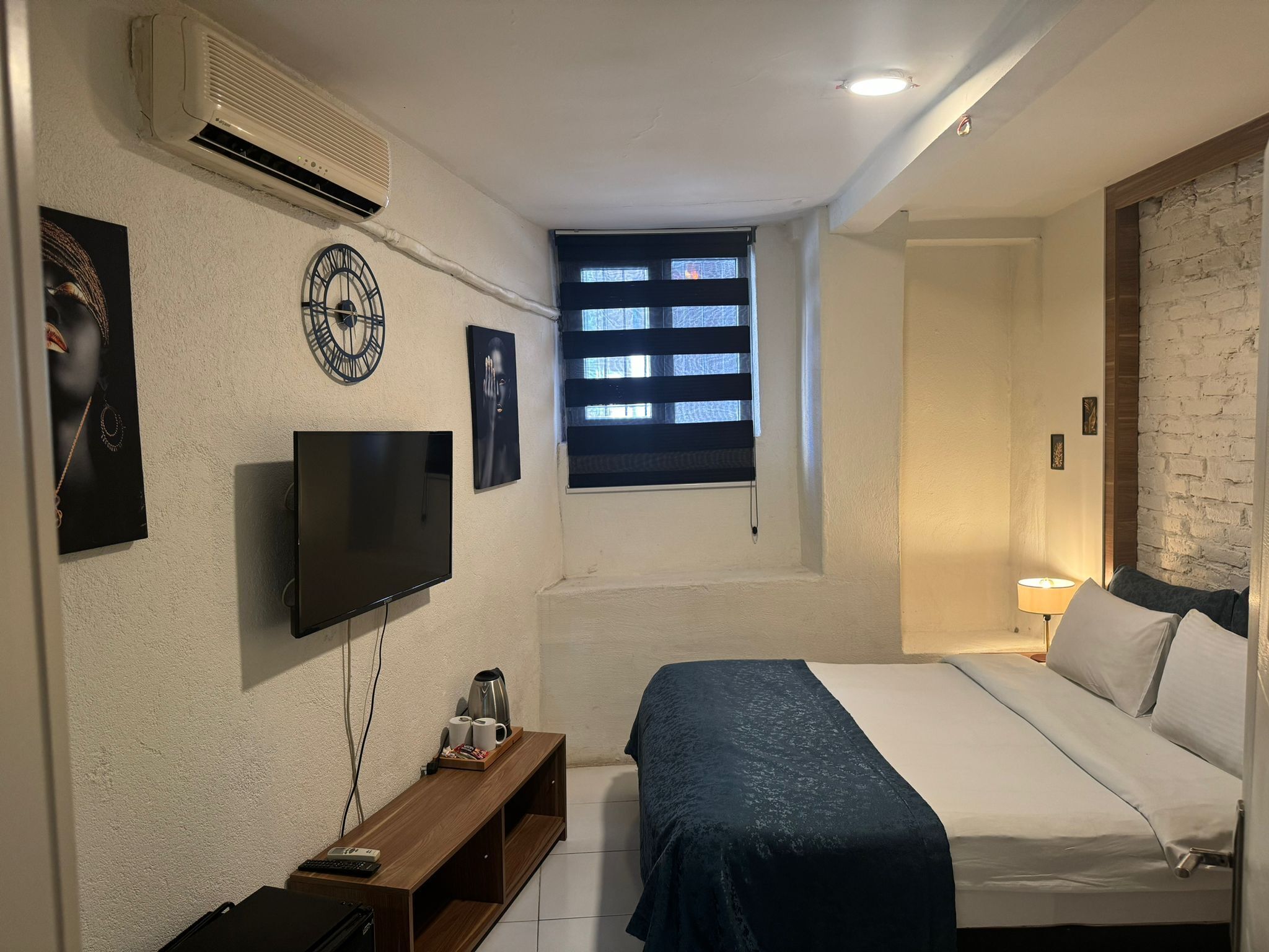 A bedroom with a bed, a TV, a coffee maker, and a window with blinds.