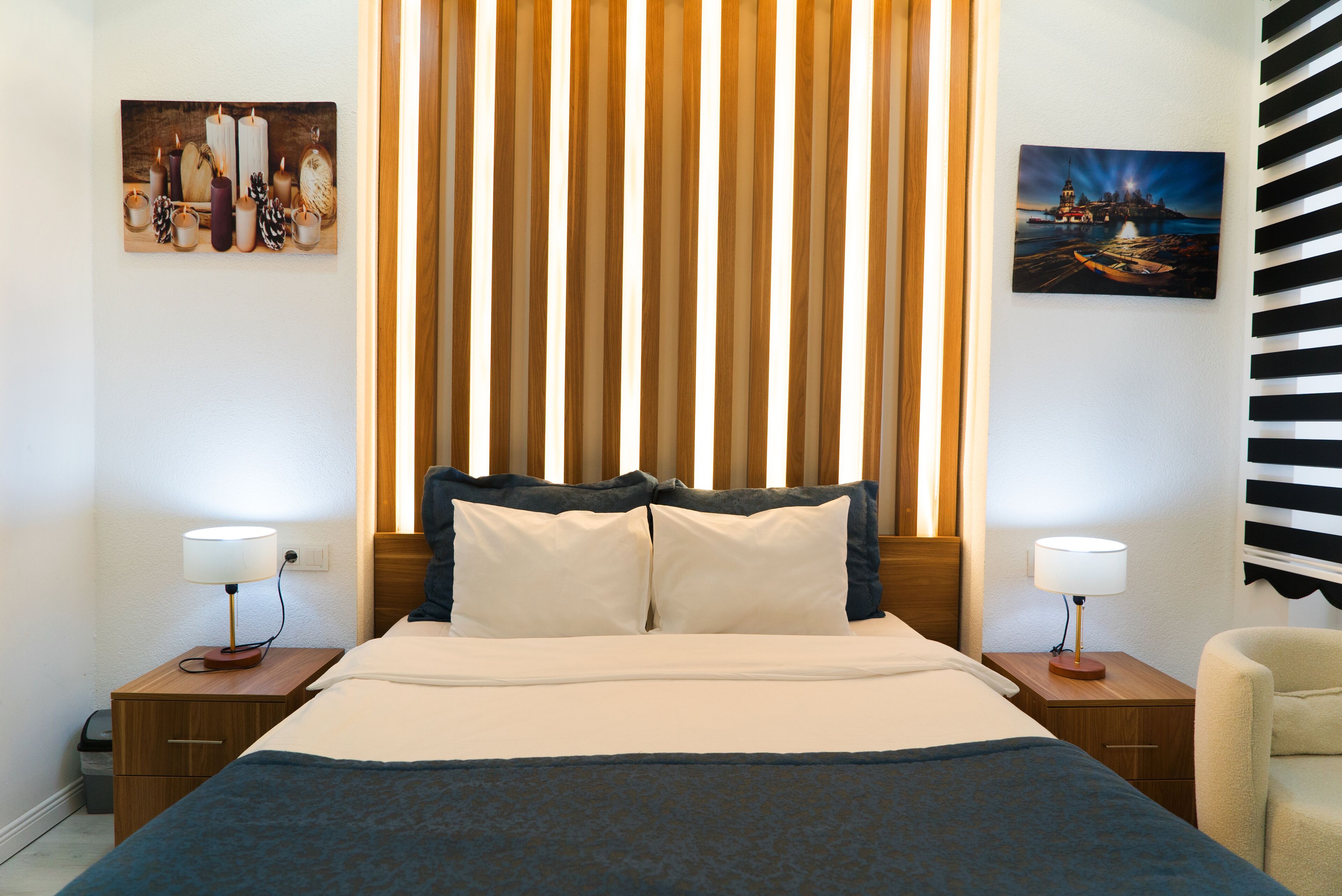 A hotel room with a bed, two bedside tables, a chair, and two paintings on the walls.
