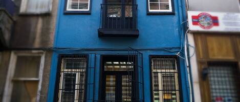 A two-story building with a blue facade, multiple windows with black grilles, and a visible sign on the right side.