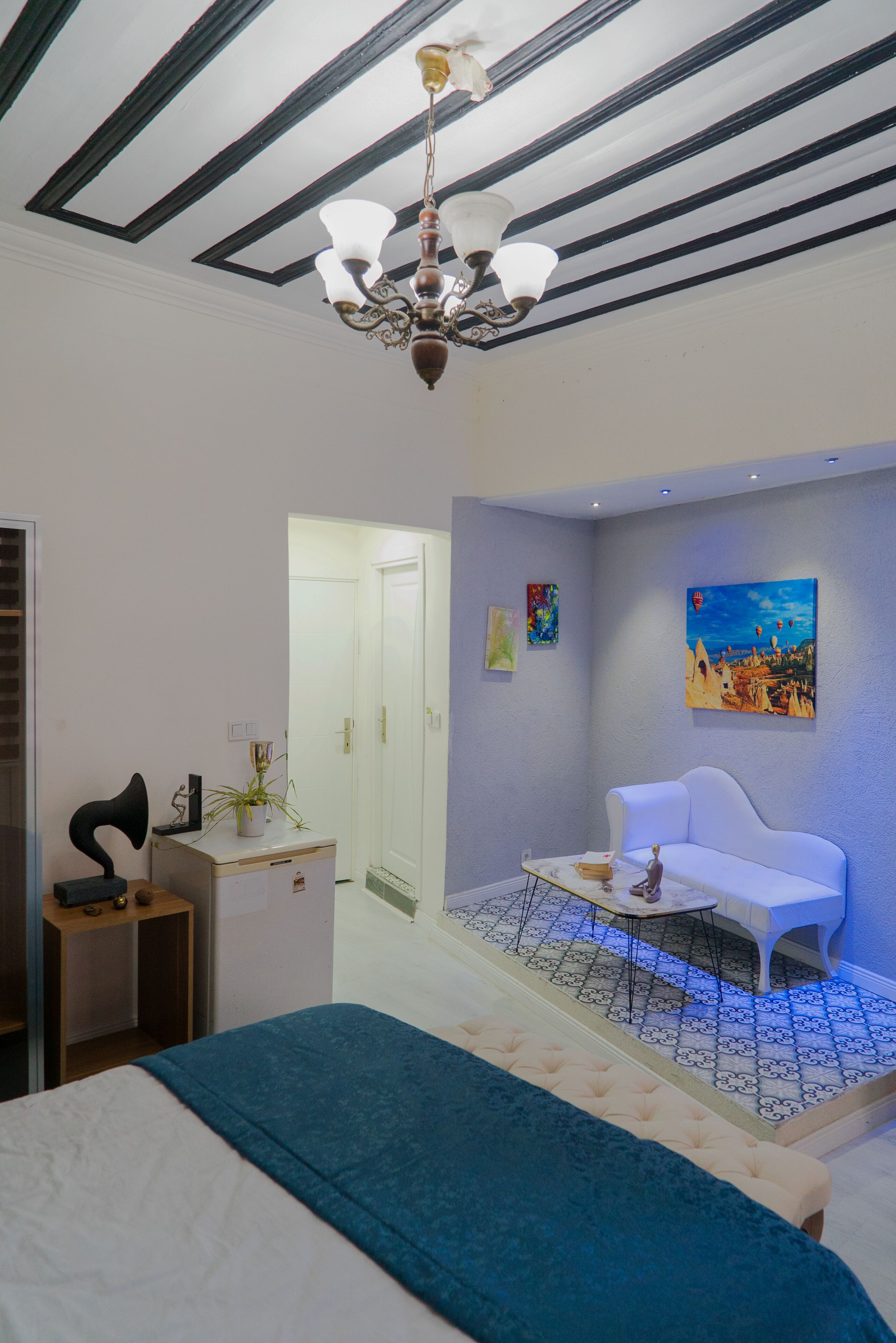 Un dormitorio con una cama, un sofá blanco, una mesita y un ventilador de techo, además de un cuadro en la pared.