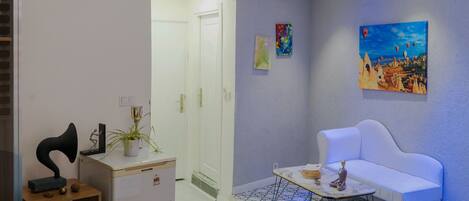 Un dormitorio con una cama, un sofá blanco, una mesita y un ventilador de techo, además de un cuadro en la pared.