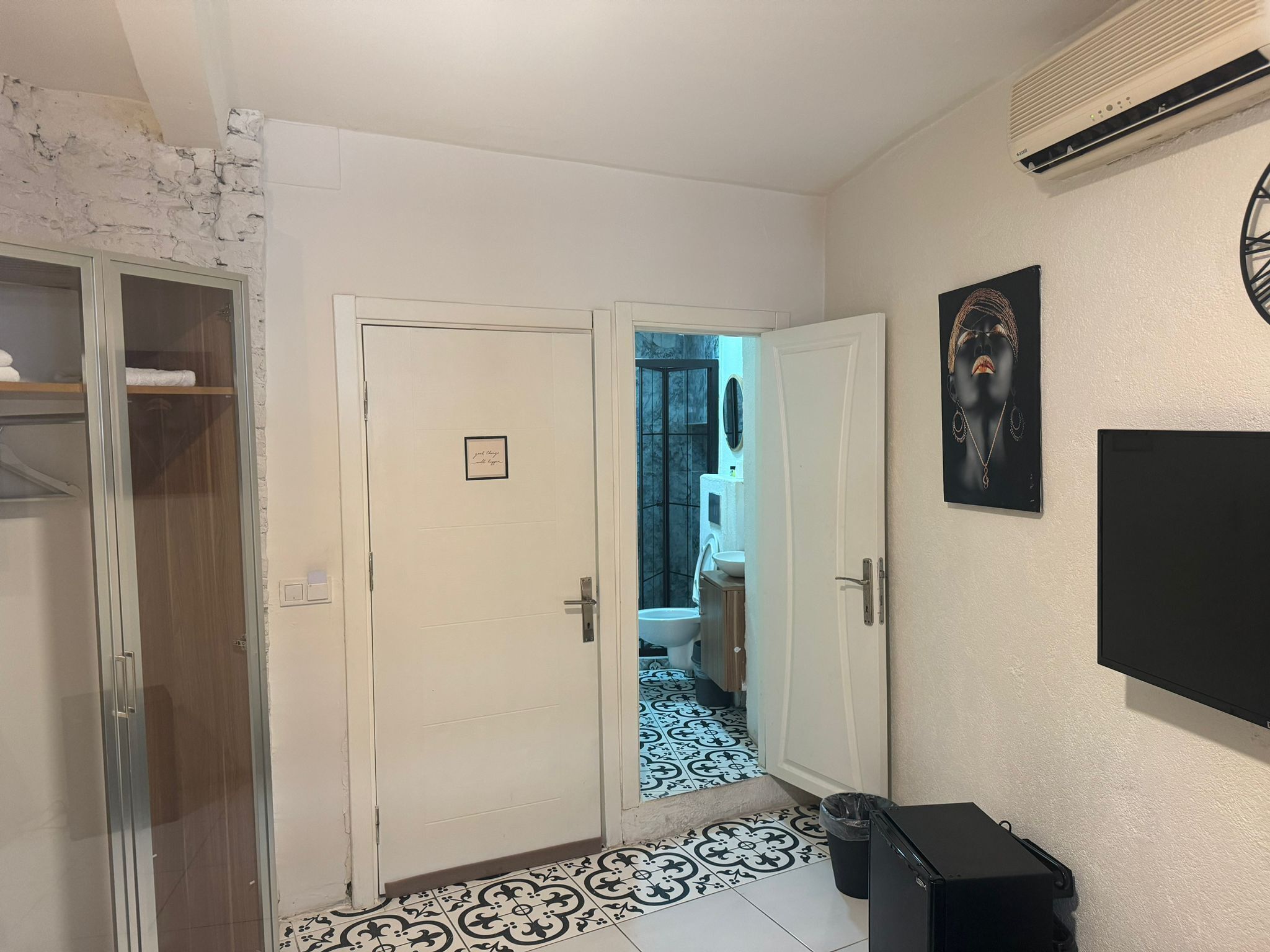 A hallway with a white door leading to a bathroom, a black trash bin, and a mounted air conditioner.