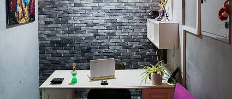 A compact living space with a desk, a purple couch, a patterned floor, a brick wall, and a staircase.