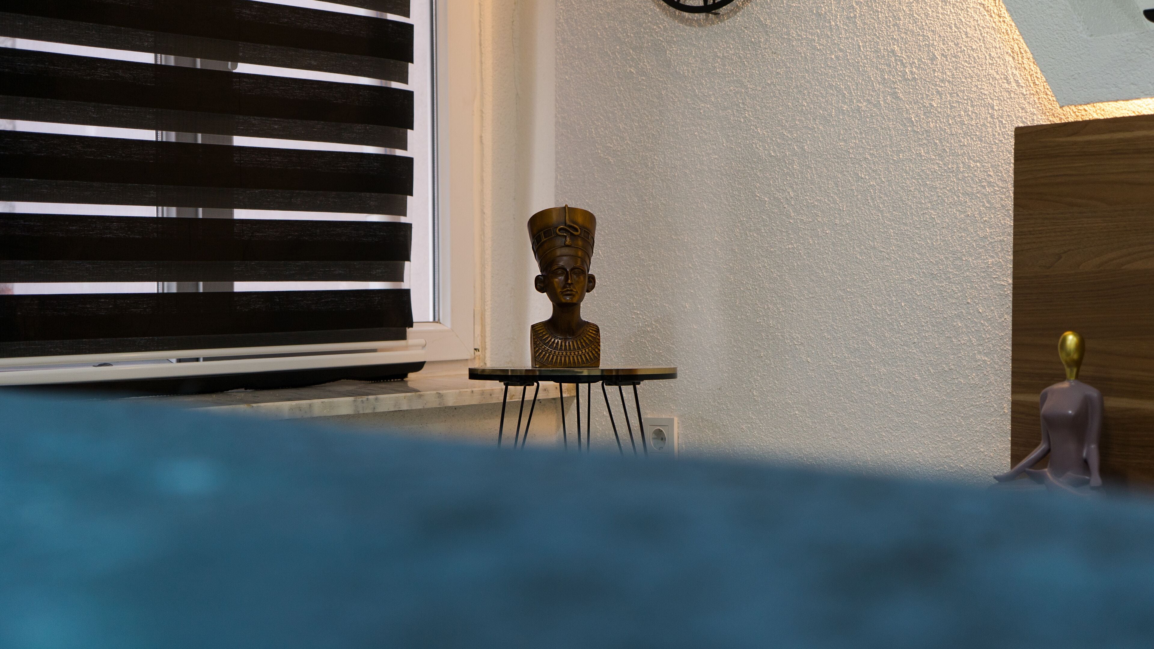 A room with a window, a small table with a bust sculpture, and a statue.