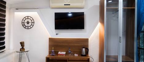 Un dormitorio con cama, televisor, armario, una mesita con objetos y un reloj de pared.