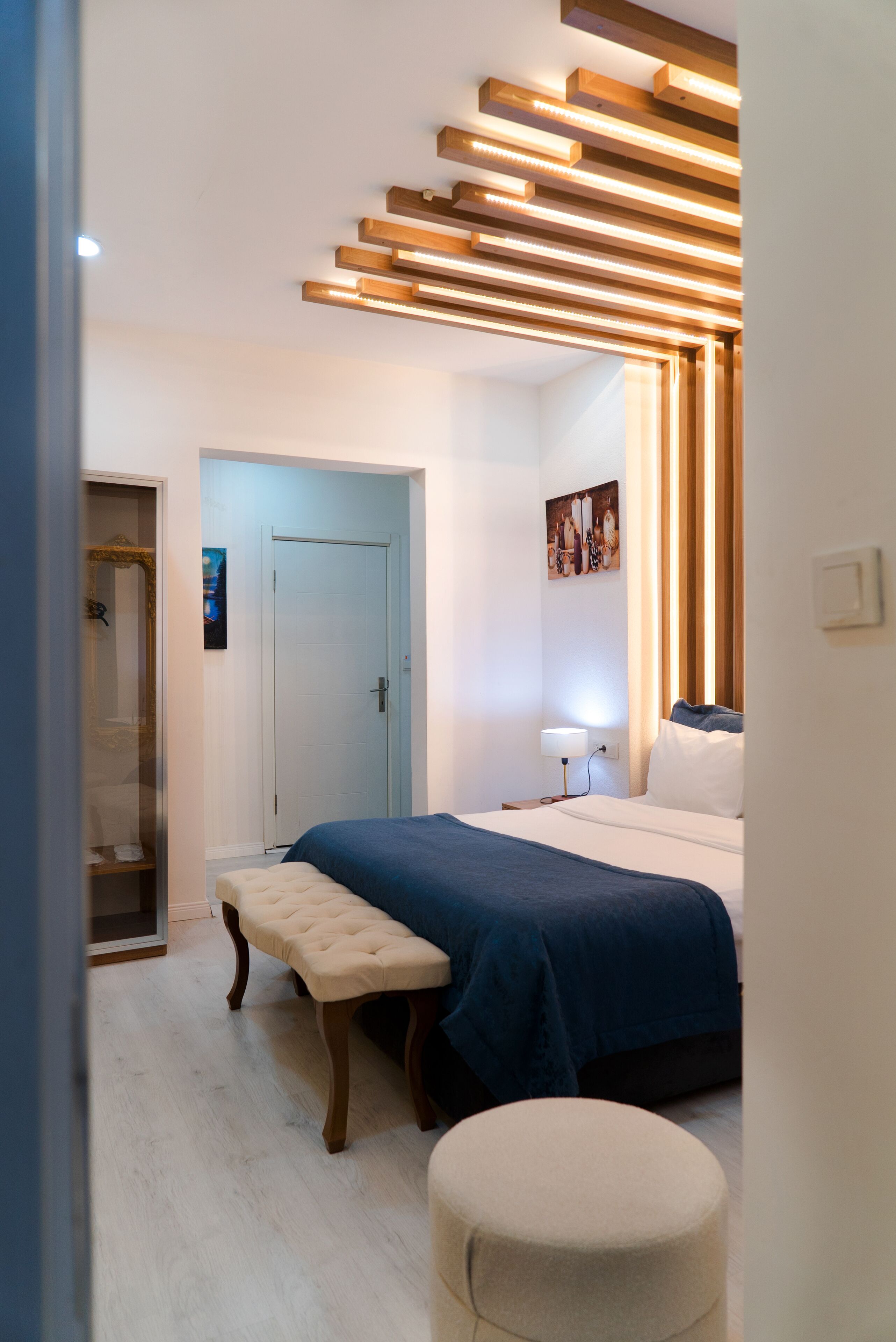 A modern bedroom with a bed, bench, ottoman, and a door leading to a bathroom.