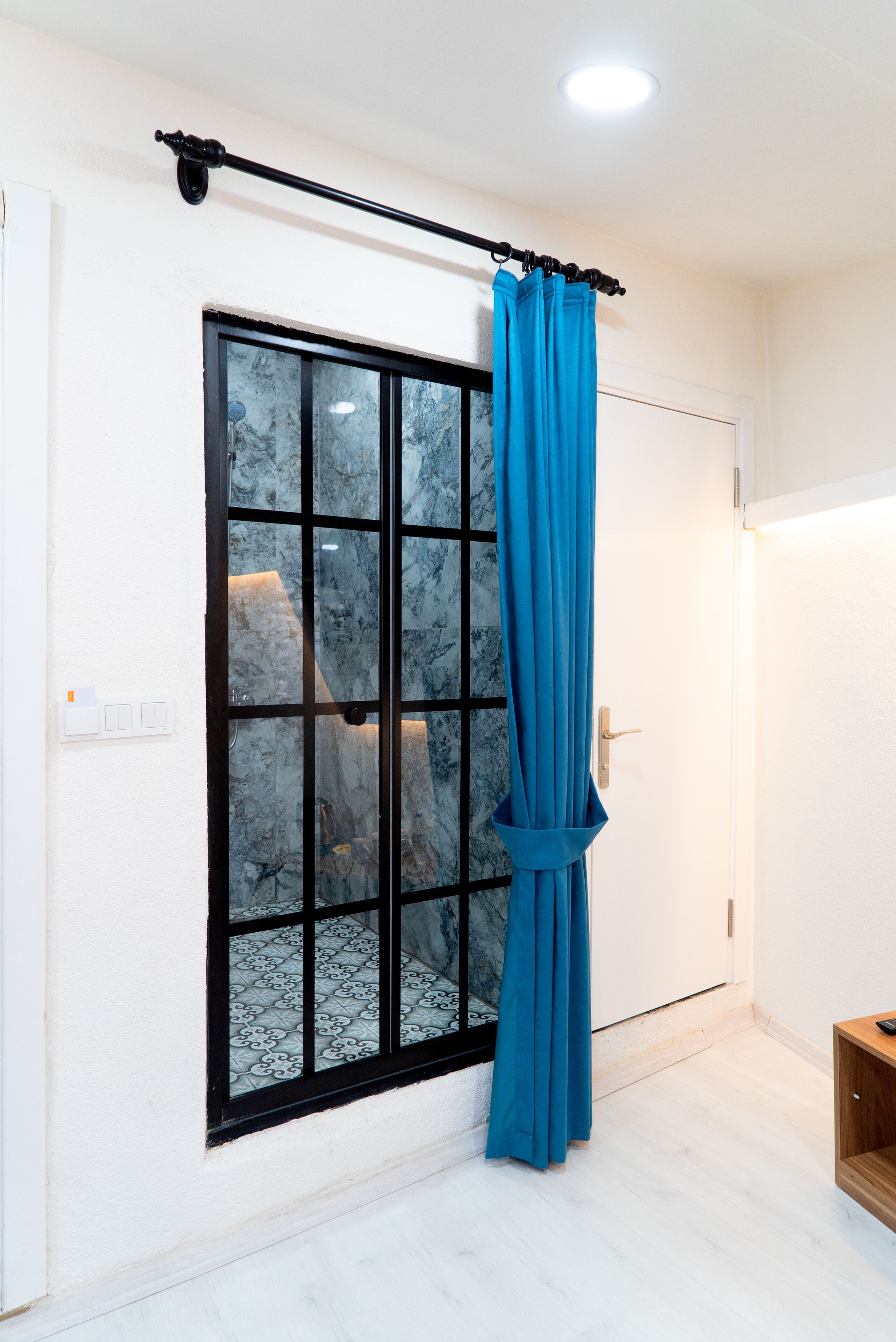 A room with a large window, a curtain rod, and a wooden shelf.