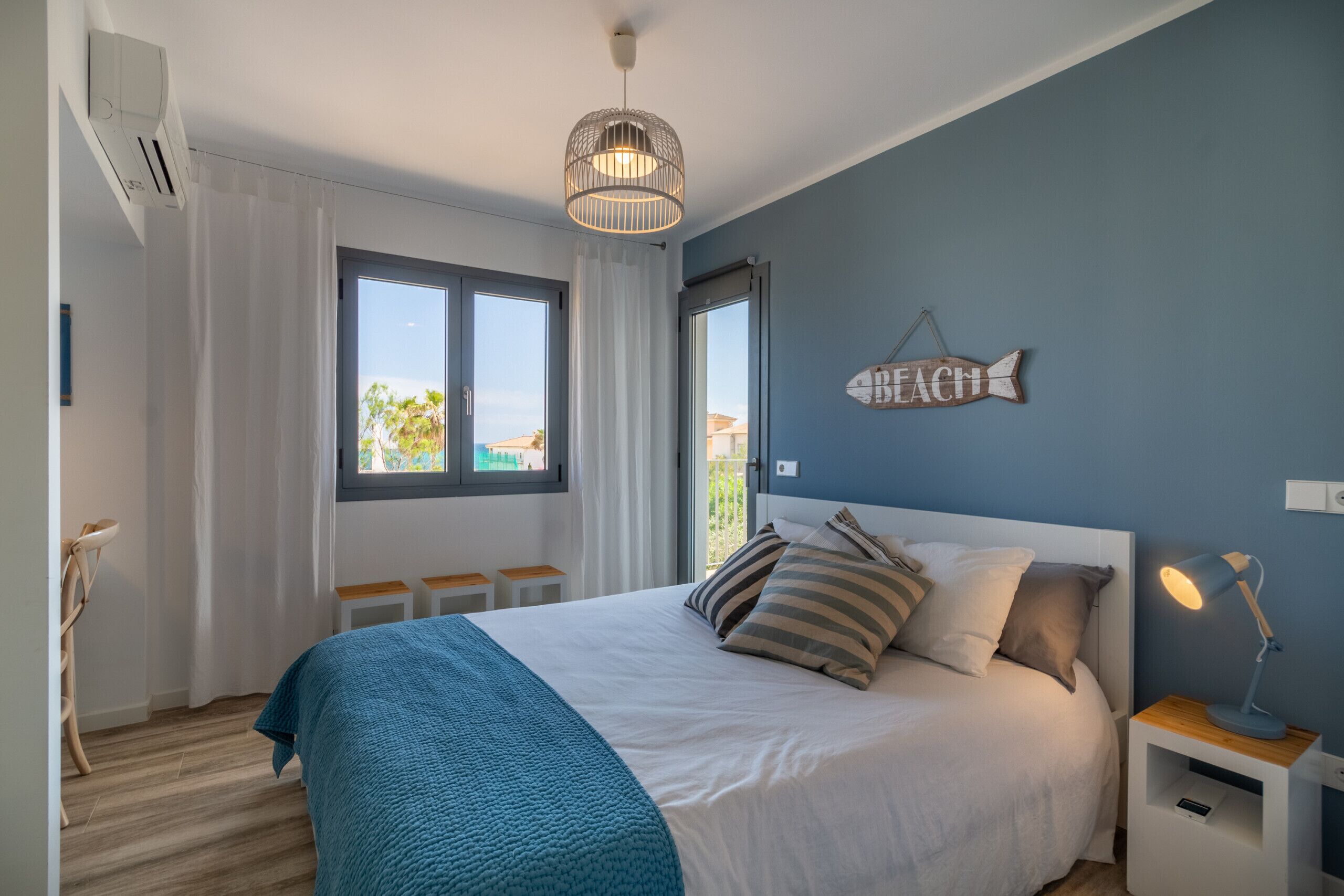 Un dormitorio con cama, mesita de noche, lámpara colgante, ventana y un adorno en la pared.