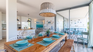 A modern dining area with a wooden table set for six, a woven pendant light, and a view through large glass doors. - Kasalmar, Beach House 5StarsHome Mallorca, private swimming pool,air,wifi,beach. (Son Serra de Marina)