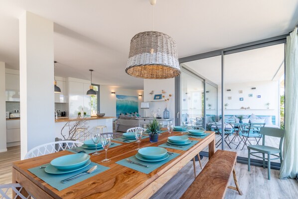 Un comedor moderno con una mesa de madera dispuesta para seis personas, una lámpara colgante tejida y vistas a través de puertas de cristal amplias.