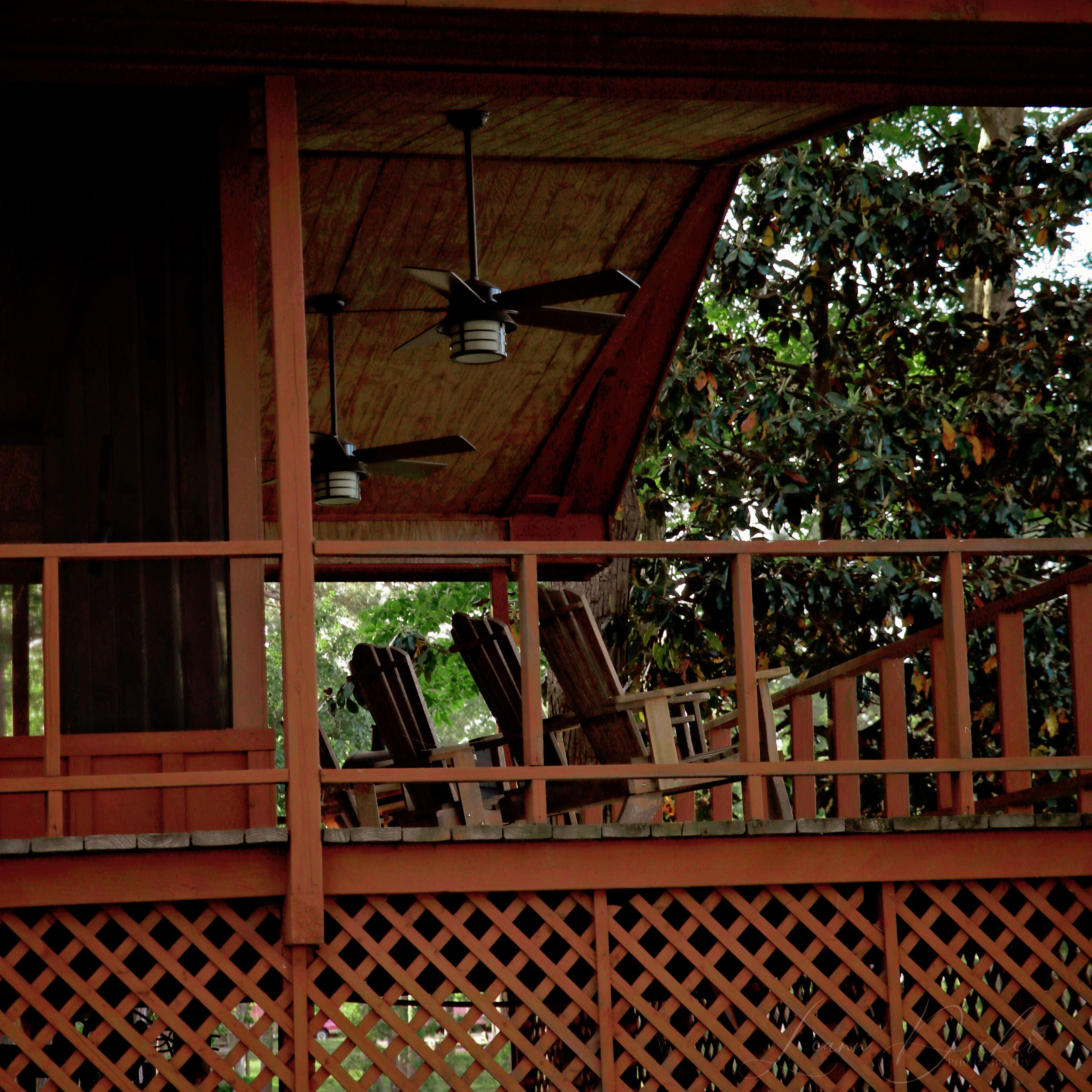 A wooden balcony with a lattice railing, ceiling fans, and a view of trees.