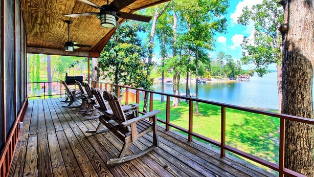 Une terrasse en bois avec des fauteuils à bascule donnant sur un lac, un plafond en bois avec un ventilateur et une vue sur les arbres et un quai.