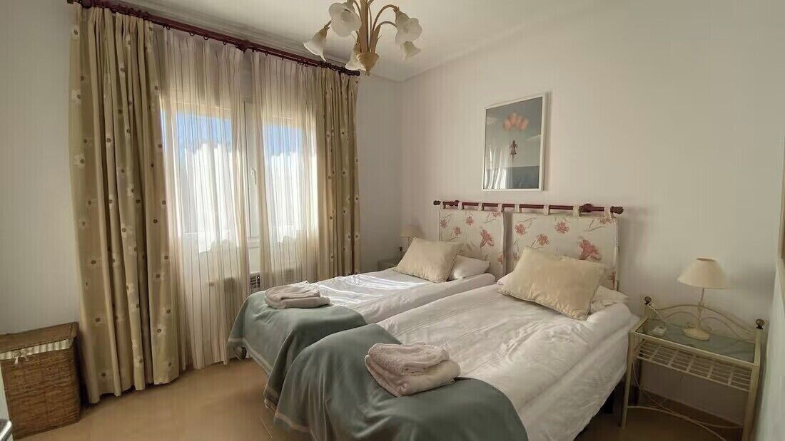A bedroom with two beds, a bedside table with a lamp, and a window with curtains.