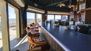 Un bar con una barra alargada, sillas de madera y vista al mar.