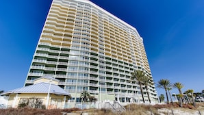 Un hotel de gran altura con varios balcones, ubicación frente a la playa y un paseo marítimo de madera.