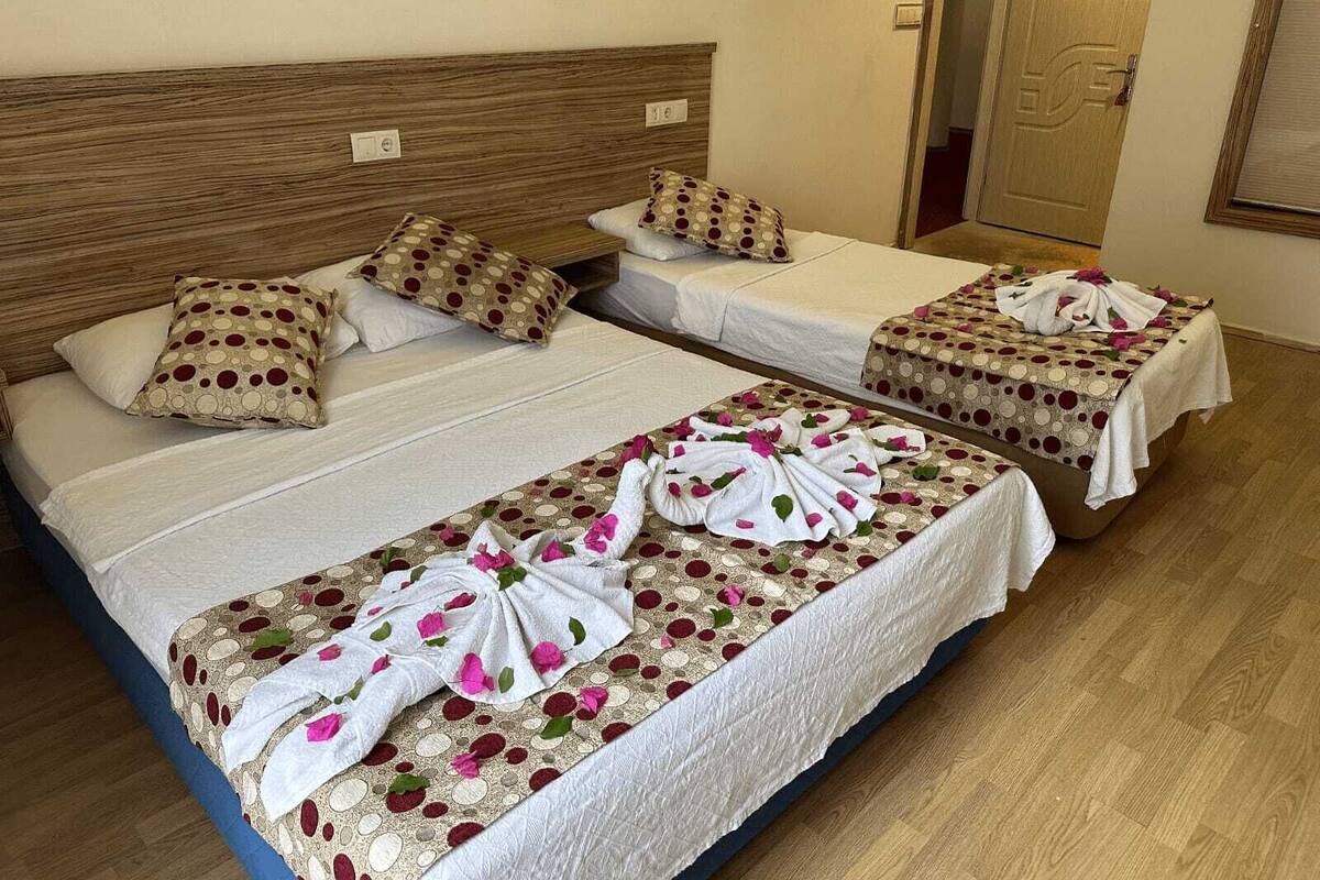 Habitación de hotel con dos camas, cada una con cabecero de madera, ropa blanca de cama y colcha con estampado floral.