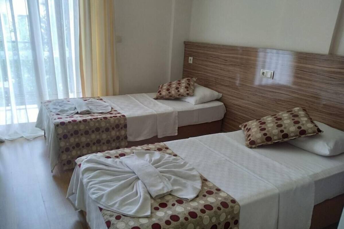 Habitación de hotel con dos camas individuales, un cabecero de madera y una ventana con cortinas.