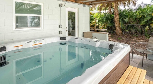 Un jacuzzi con una terraza de madera y una pared exterior blanca.
