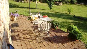 Un patio al aire libre con una mesa preparada para dos, una silla y una mesita con una botella y vasos.