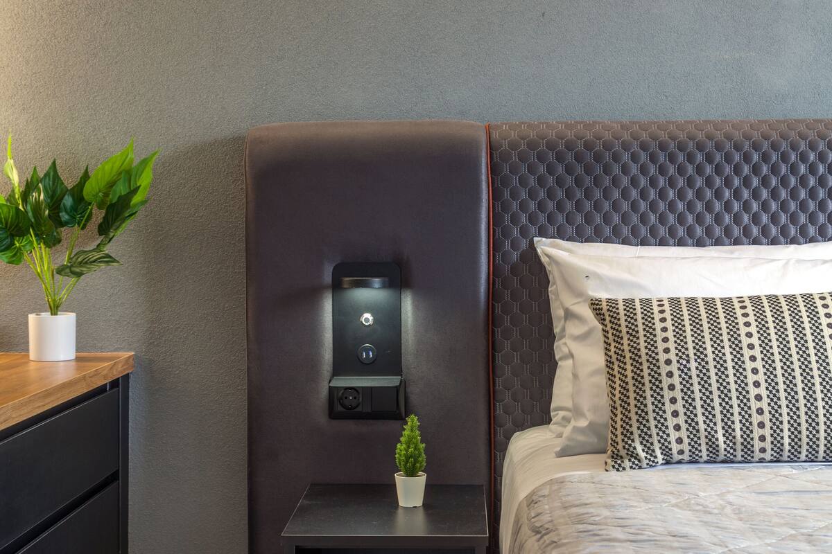 Une chambre d’hôtel moderne, équipée d’un lit, d’une table de chevet, d’une petite plante en pot et d’un panneau de commande sur la table de chevet.