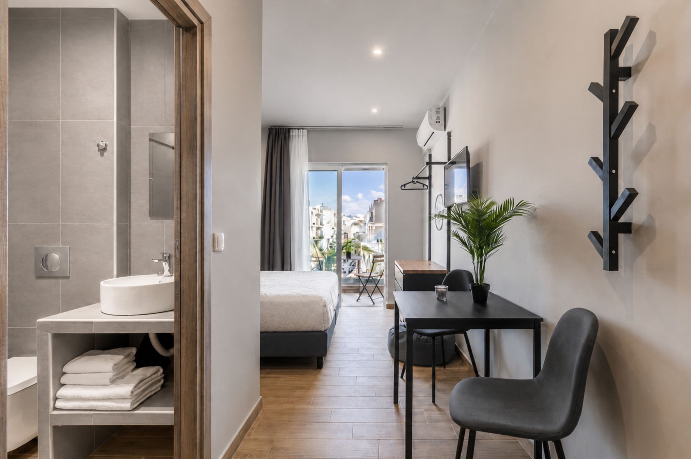Ein modernes Hotelzimmer mit Bad, Bett, Schreibtisch und Stuhl.