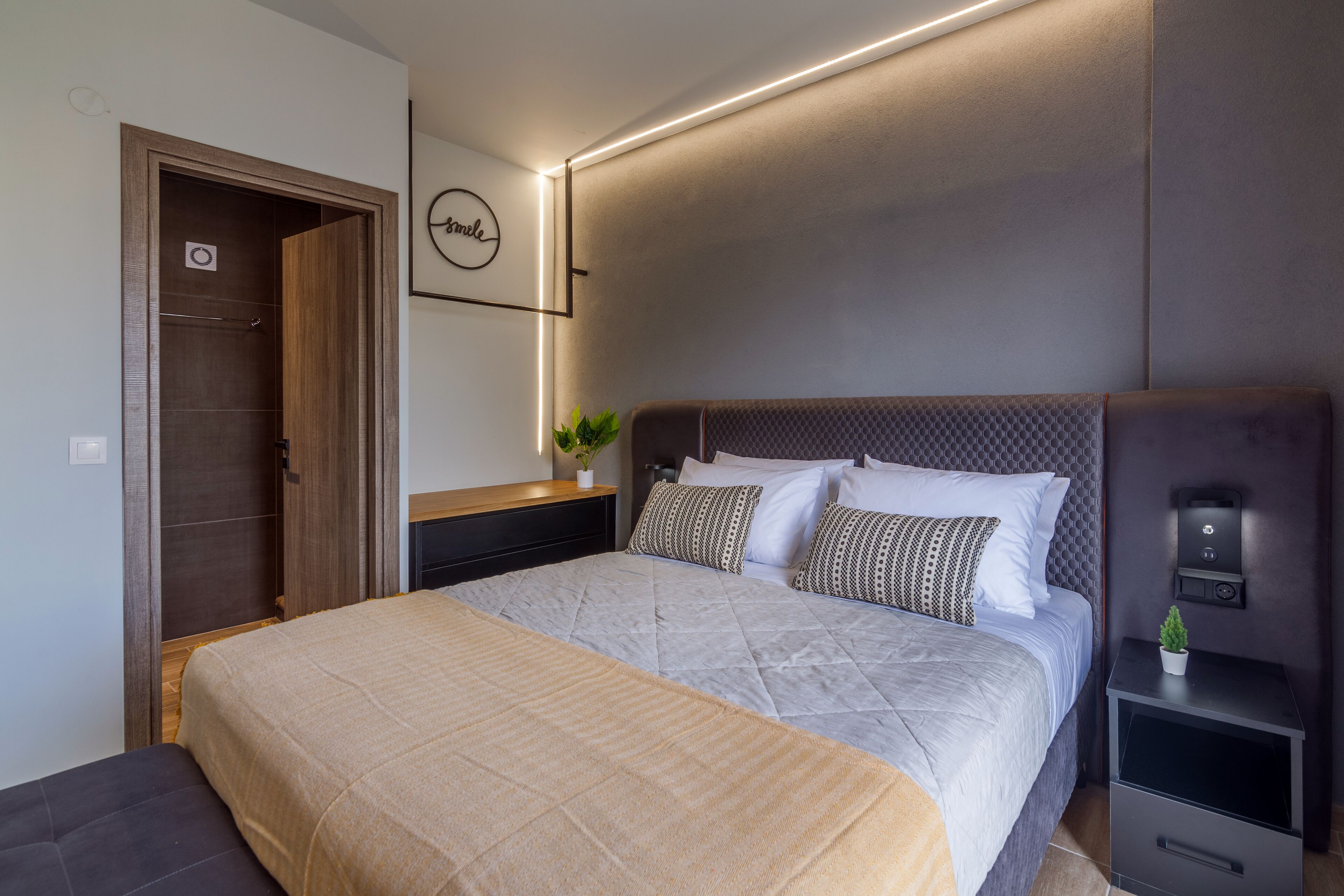Een moderne slaapkamer met een groot bed, een nachtkastje met een plant en een wandlamp.