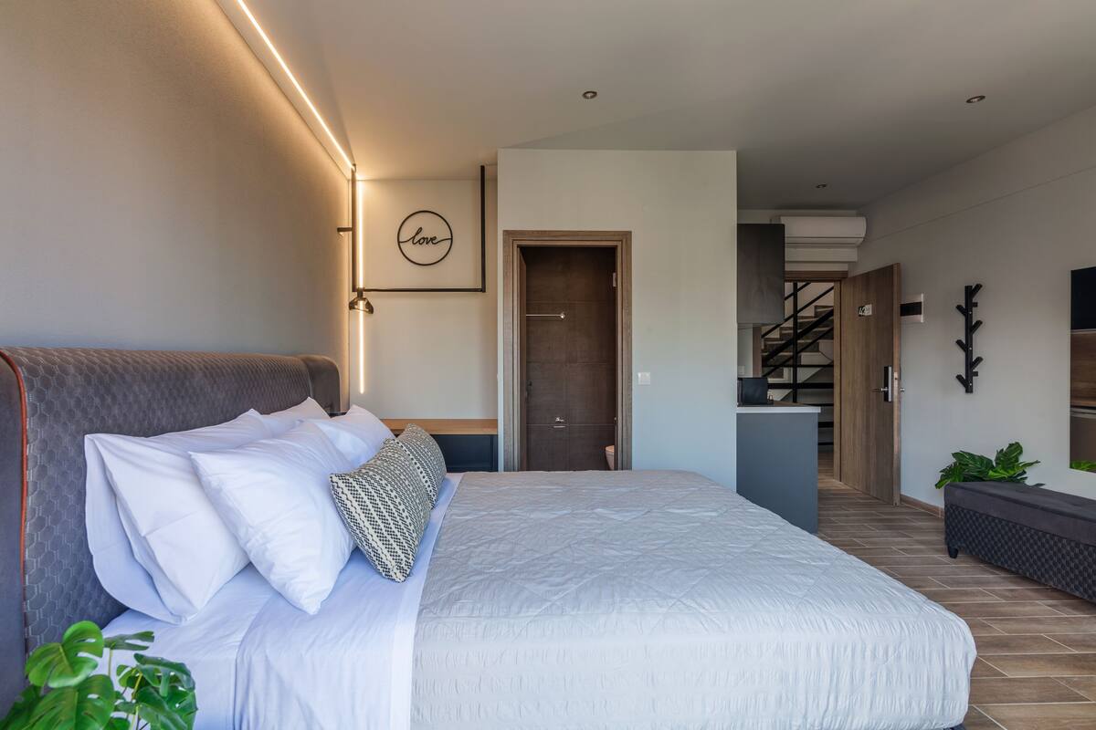 Une chambre moderne avec un grand lit, une table de chevet, une lampe fixée au mur et une porte donnant sur un escalier.
