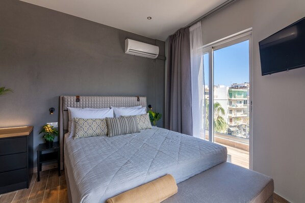 A modern bedroom with a large bed, a TV, and a city view.