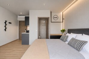 Une chambre moderne avec un grand lit, une table de chevet, une commode, une lampe fixée au mur et un tableau encadré.