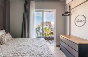 Una camera da letto con un letto, una scrivania, una sedia e un balcone affacciato su edifici.