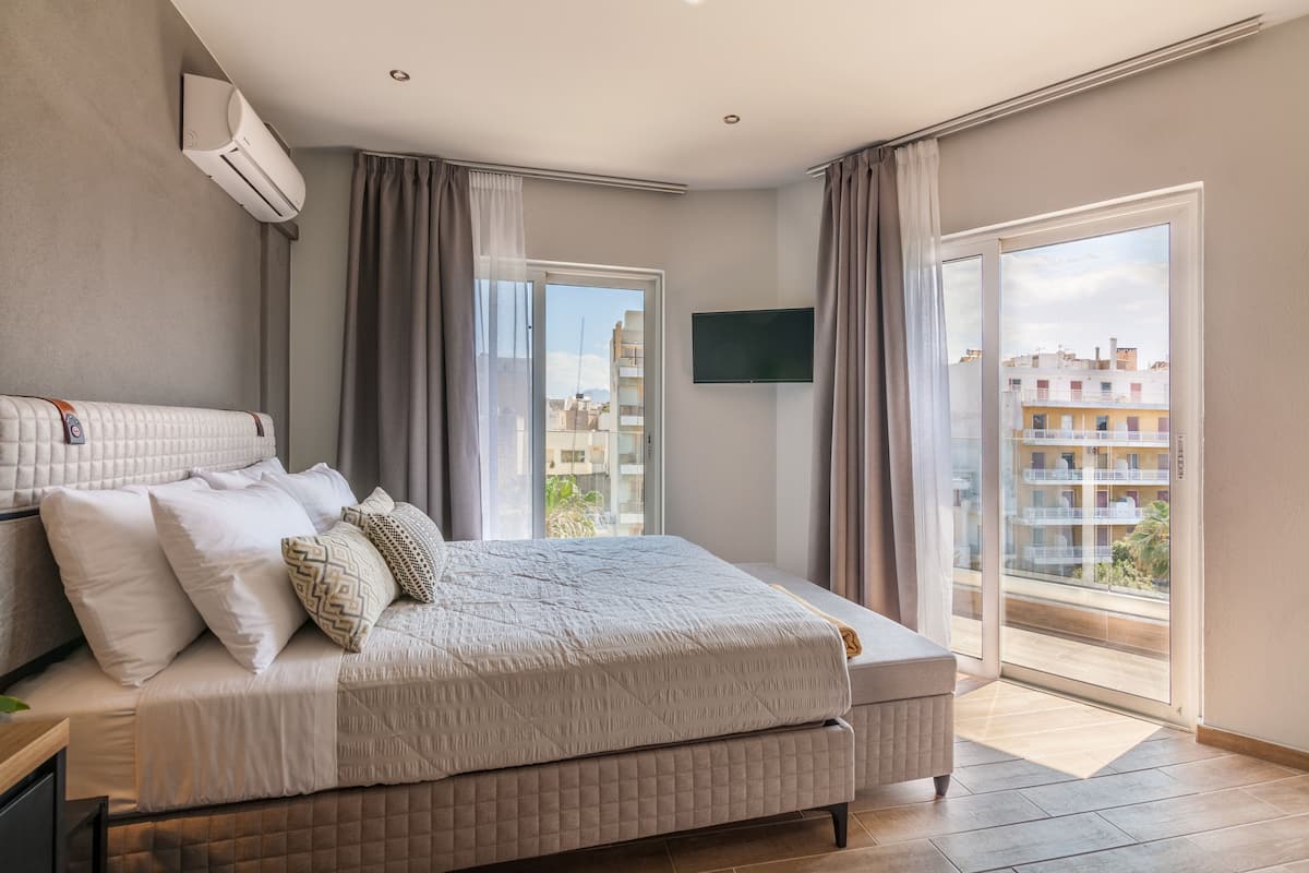 Une chambre moderne dotée d’un grand lit, d’un téléviseur à écran plat et d’un balcon offrant une vue sur la ville.