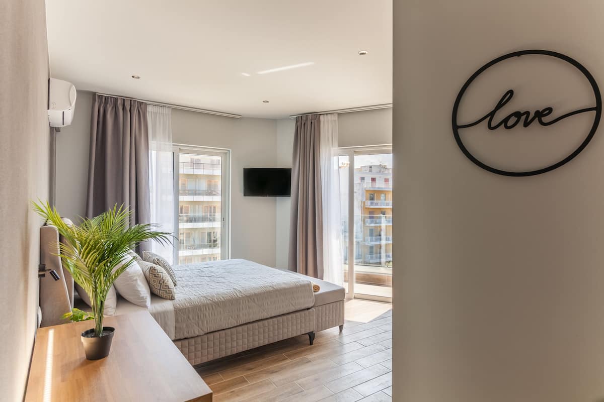 Une chambre à coucher moderne avec un lit, une plante en pot, un téléviseur fixé au mur et un panneau décoratif portant le mot « amour ».