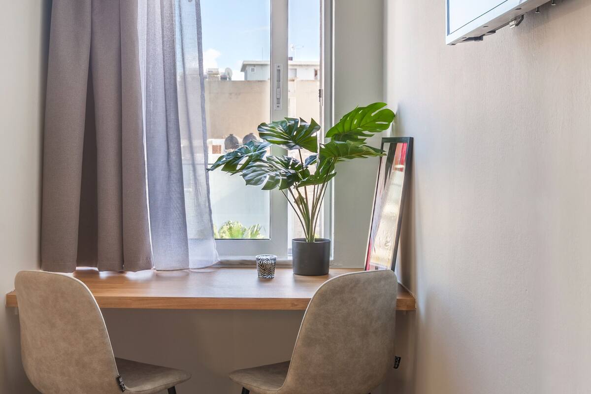 Une petite pièce moderne, avec un bureau en bois, deux chaises, une plante en pot et un pouf jaune.