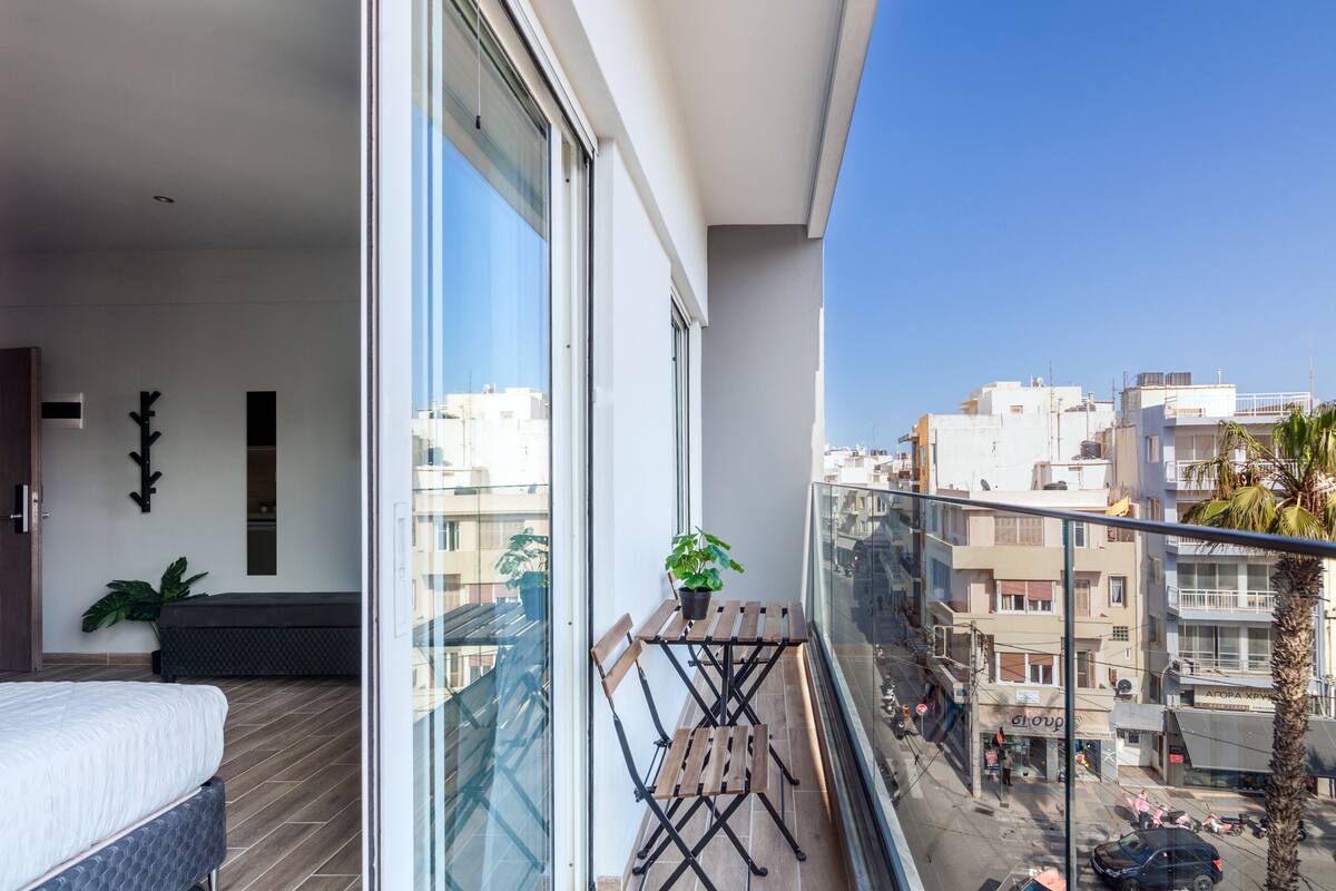 Un balcon avec une table et des chaises en bois, un pot de fleurs et une vue sur le paysage urbain.