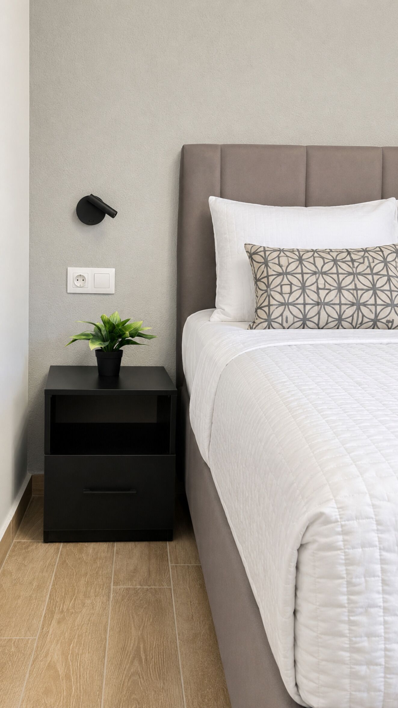Un dormitorio ordenado con cama, mesita de noche y un aplique de pared.