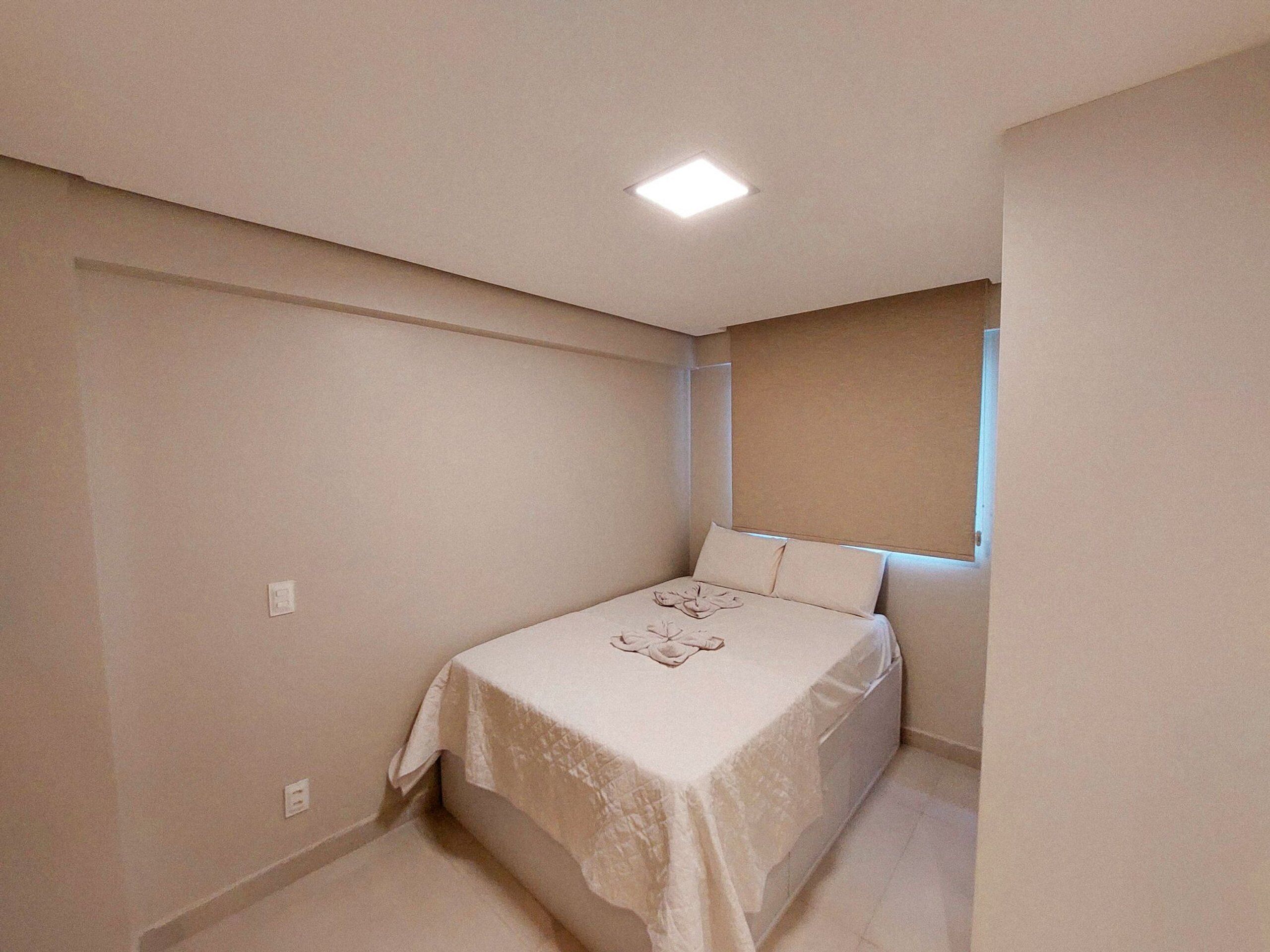 A small, neatly arranged bedroom with a single bed, a window, and a ceiling light.