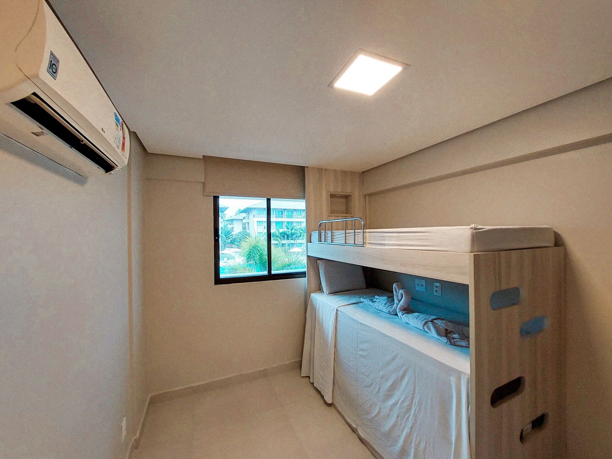 A small, compact room with bunk beds, a window, and an air conditioning unit.