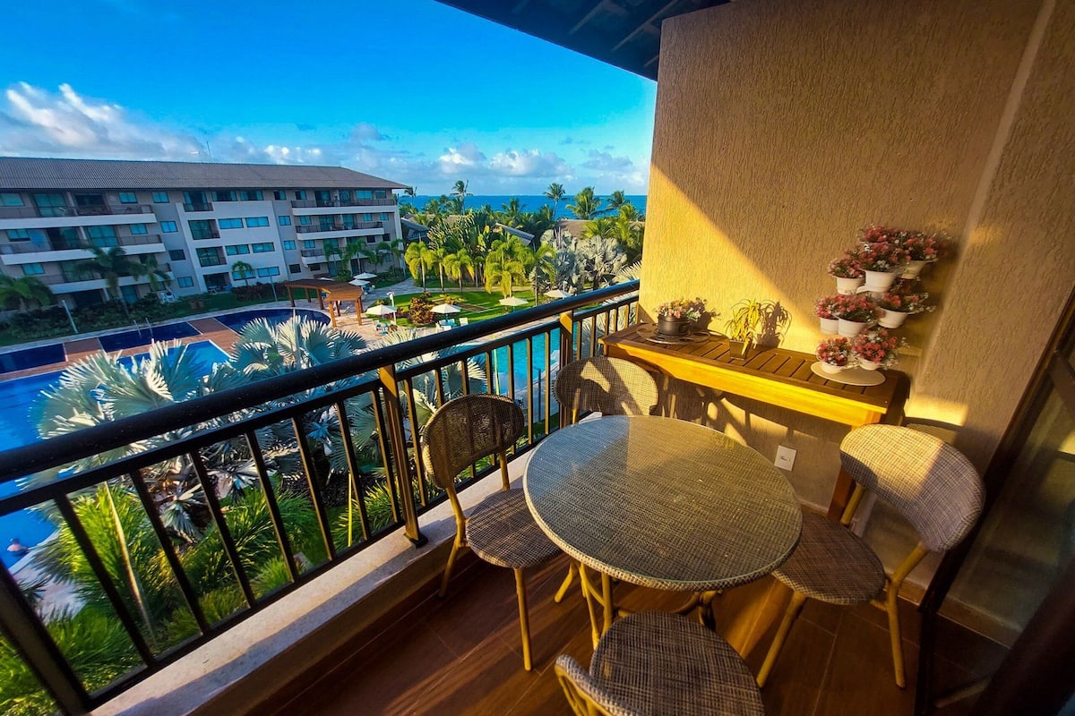 Un balcon agrémenté de meubles en osier, d’une petite table et de plantes en pot.