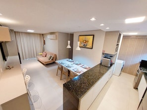 A modern apartment with a dining area, kitchenette, and a living space with a sofa and curtains. - Beach Class Residence Eco Life (Ipojuca)
