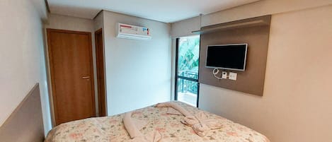 A bedroom with a bed, a TV mounted on the wall, and a window with a view of a balcony.