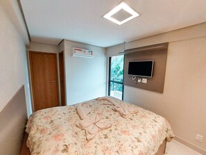 Ein Schlafzimmer mit einem Bett, einem an der Wand montierten Fernseher und einem Fenster mit Blick auf einen Balkon.