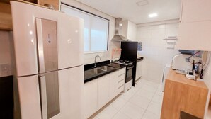 A modern kitchen with white cabinets, a stainless steel refrigerator, a black countertop, and a built-in oven. - Beach Class Residence Eco Life (Ipojuca)