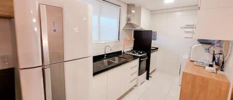 A modern kitchen with white cabinets, a stainless steel refrigerator, a black countertop, and a built-in oven.