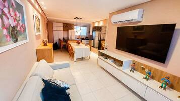 A modern living room with a sofa, TV, and a dining area in the background.