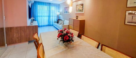 Un comedor con una mesa dispuesta para cuatro, un jarrón de flores y vistas al salón a través de un ventanal.