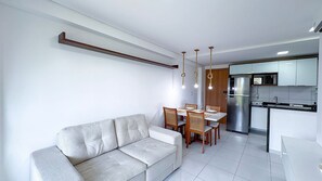 Ein modernes Wohnzimmer mit Sofa, Esstisch, Stühlen und einer Küchenzeile mit Kühlschrank.