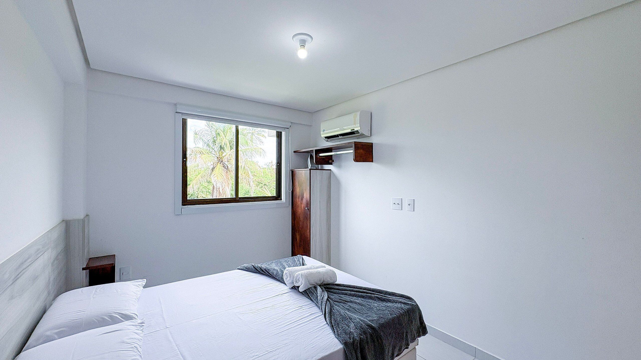 Un dormitorio con cama, ventana, armario y luz en el techo.