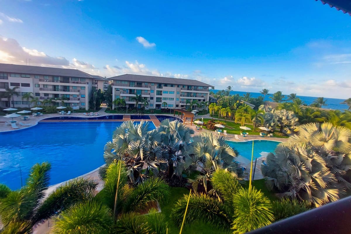 A resort with a large swimming pool, multiple hotel buildings, and palm trees.