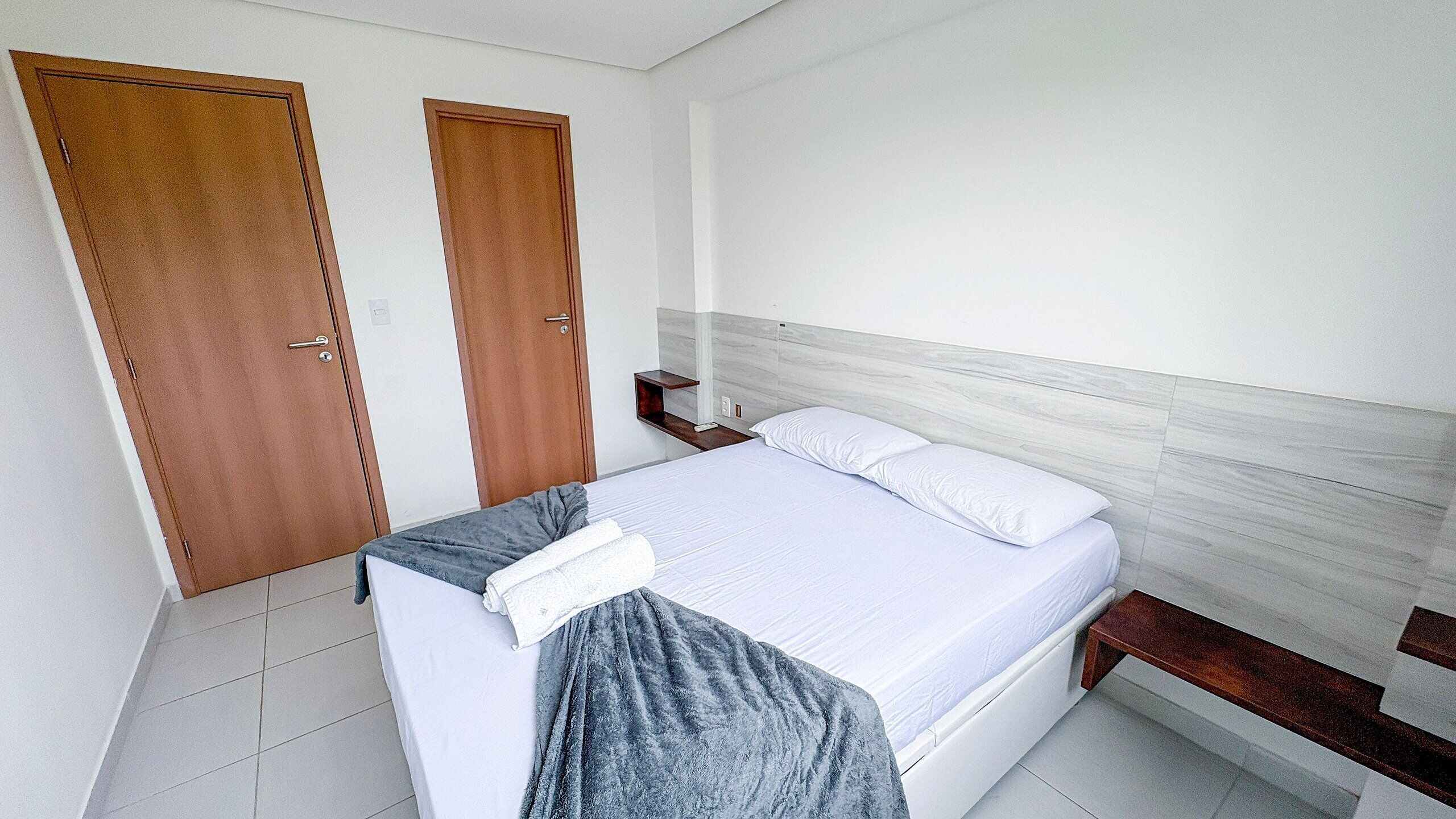 A bedroom with a bed, two wooden doors, a bedside table, and a nightstand.